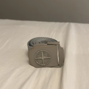 Grått bälte från Stone Island - Ett grått skärp ifrån Stine Island. Skärpet har jag haft i många år och använder inte längre. Som ni ser är märket ganska utslitet och lite färg har börjat tappats. Själva bältet är i ganska bra skick. 100 cm. Nypris runt 1100, mitt pris 450😮‍💨💯😍. Skriv vid frågor!