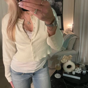 Vit ribbad kofta - Säljer en stilren vit ribbad kofta med knappar framtill. Koftan har långa ärmar och en croppad passform, perfekt för lager-på-lager-stil. Passar bra till både jeans och kjol.