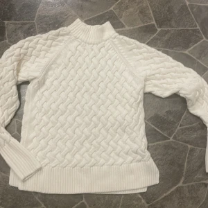 Vit stickad tröja - Säljer en stilren vit stickad tröja med ett snyggt flätmönster. Tröjan har långa ärmar och ribbade muddar vid ärmslut och nederkant. Perfekt för kyliga dagar!