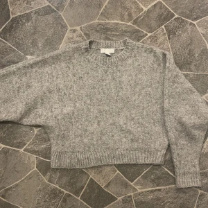 Grå stickad tröja från H&M - Mysig grå stickad tröja från H&M i storlek XS. Perfekt för kyliga dagar med sin ribbade rundhals och långa ärmar. Enkel och stilren design som passar till det mesta.