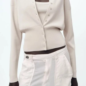 Beige kofta från ZARA - Snygg beige kofta från ZARA med knappar framtill. Den har en ribbad nederdel och långa ärmar, perfekt för en stilren look. Passar bra till både vardag och mer uppklädda tillfällen.