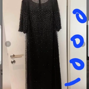 Svart långklänning med pärlor - Elegant svart långklänning dekorerad med pärlor över hela tyget. Klänningen har trekvartsärmar och en rund halsringning. XL.