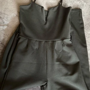 Svart jumpsuit med smala axelband - Elegant svart jumpsuit med smala axelband och v-ringad hals. Perfekt för en stilren look. Materialet är mjukt och bekvämt, vilket gör den idealisk för både vardag och festligare tillfällen.