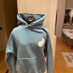 Our legacy workshop hoodie - Säljer en blå hoodie med en stor ficka fram och texten 'WORK SHOP' tryckt på baksidan. Den har en stor luva och ett litet cirkulärt mönster på bröstet. Perfekt för en avslappnad stil.