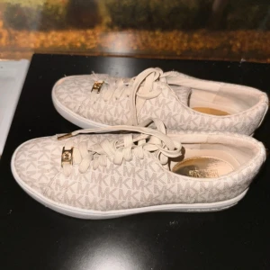 Beige sneakers från Michael Kors - Snygga beige sneakers från Michael Kors med det ikoniska MK-mönstret. Skorna har snörning och en dekorativ logga på hälen. 