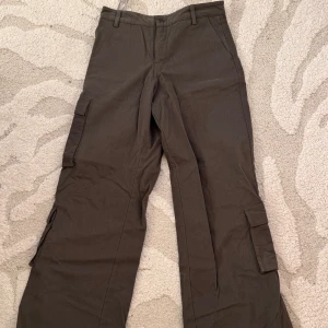 Khaki cargopants från Motel Rocks - Säljer ett par khaki cargopants med flera praktiska fickor på sidorna. Byxorna har en normal passform och är perfekta för en avslappnad stil. De har bälteshällor och stängs med knapp och dragkedja. Jag har aldrig haft på mig dom - tag kvar.