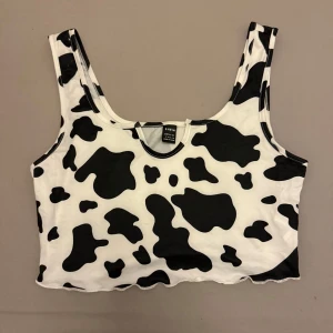 Svartvitt linne - Trendig svartvit linne med koskinnsmönster. Perfekt för en djärv och lekfull stil. Linnet är ärmlöst och har en rund halsringning.