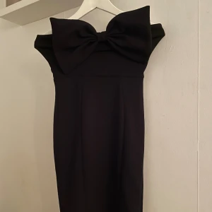 Svart klänning med stor rosett från H&M - Elegant svart klänning från H&M med en stor rosett framtill. Klänningen är axelbandslös och har en dragkedja i ryggen för enkel påklädning. Perfekt för en stilren look och nu till nyår 