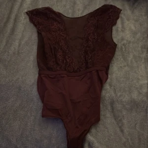 Vinröd spetsbody - Snygg vinröd body med djup v-ringning och spetsdetaljer. Perfekt för en elegant look. Ärmlös design med en smickrande passform.