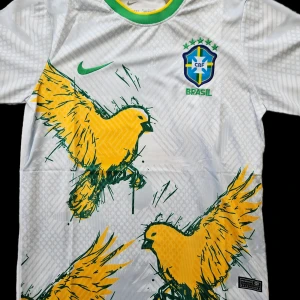 Vit Brasilien fotbollströja med gul fågel - Snygg vit fotbollströja från Nike med Brasilien-emblem och stora gula fåglar på framsidan. Tröjan har korta ärmar och gröna detaljer vid kragen. Perfekt för fotbollsfans som vill sticka ut!