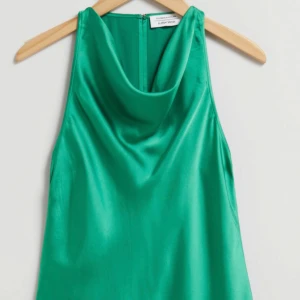 Grön ärmlös topp från & Other Stories - Snygg grön ärmlös topp i satin från & Other Stories. Toppen har en elegant drapering vid halsen och en diskret dragkedja i ryggen. Perfekt för en stilren look. Skicka för mer bilder.