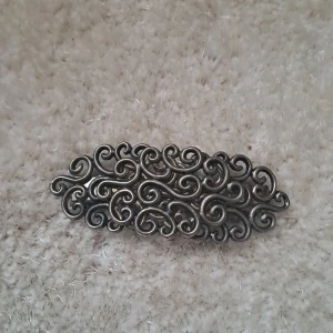 Silverfärgad hårklämma med snirkligt mönster - Elegant hårklämma i silverfärg med ett vackert snirkligt mönster. Perfekt för att ge en stilfull touch till din frisyr. Klämman är robust och håller håret på plats hela dagen.