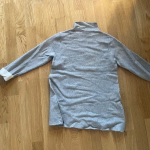 Grå polotröja från Tahari - Säljer en stilren grå polotröja från Tahari. Tröjan har 3/4 långa ärmar och en dragkedja på sidan för extra stil och komfort. Perfekt för kyligare dagar.