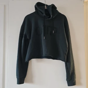 Svart croppad hoodie från OTP - Säljer en svart croppad hoodie från OTP. Den har en stor huva med dragsko och långa ärmar. Materialet är en blandning av bomull och polyester vilket gör den mjuk och bekväm. Perfekt för en avslappnad stil.