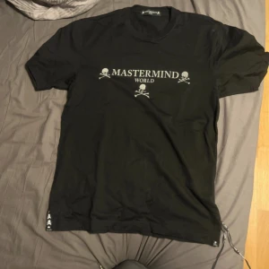 Svart t-shirt från Mastermind World - Snygg svart t-shirt från Mastermind World med deras ikoniska dödskallelogga och text på framsidan. T-shirten har korta ärmar och en normal passform. Perfekt för en stilren look.