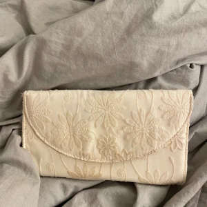 Beige broderad kuvertväska - Elegant beige kuvertväska med vackert broderade blommor. Den är använd 1 gång och är i bra skick! 