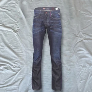 Mörkblå jeans från replay - Snygga mörkblå jeans från replay med klassisk femficksdesign och knappgylf. Jeansen har en straight passform och är perfekta för en avslappnad stil. De har en diskret logga på bakfickan och är tillverkade i slitstarkt denim. Storlek w33 snygga modell Waitom så lite med straight jeans säljs inte längre därav priset 