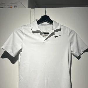 Vit Dri-FIT pikétröja från Nike - Säljer en vit Dri-FIT pikétröja från Nike Golf. Tröjan har korta ärmar och en klassisk krage med knappar. Perfekt för sportiga aktiviteter med sin bekväma passform och fukttransporterande material. Perfekt för en tränings dag eller en golf dag 