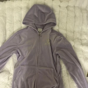 Lila hoodie från Juicy Couture - Säljer en lila Juicy Couture hoodie med dragkedja och huva. Den har JC-märke på bröstet och Juicy Couture-logga på ryggen. Perfekt för en avslappnad stil. 🧥✨passar mig som vanligtvis använder xs.