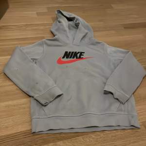 Säljer en grå hoodie från Nike med det klassiska logotyptrycket i svart och rött på framsidan. Tröjan har en bekväm huva och långa ärmar. Perfekt för en avslappnad stil.