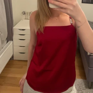 Röd satinlinne - Snygg röd satinlinne med tunna axelband. Perfekt för en stilren look. Linnet har en enkel och elegant design som passar till många tillfällen.