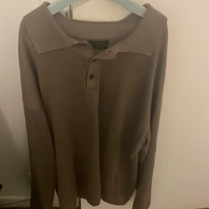 Brun långärmad tröja från Massimo Dutti - Säljer en stilren brun långärmad tröja från Massimo Dutti. Tröjan har en klassisk krage och knappar framtill. Perfekt för en avslappnad men ändå elegant look.