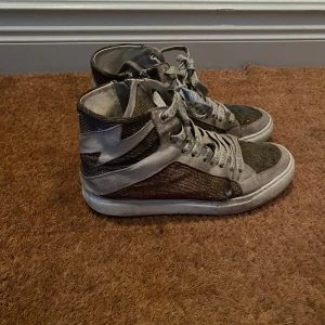 Glittriga sneakers från Zadig & Voltaire - Snygga sneakers från Zadig & Voltaire med glittriga detaljer i guld. Skorna har en hög modell med snörning och en stjärndetalj på sidan. Använt mycket där av priset, dessvärre har ena  sulan gått av ses  på sista bilden men det är inget problem att gå i dom men annars kan man lämna in till en skräddare och få sulan omgjord och även laga de tre små hålen fram till❤️