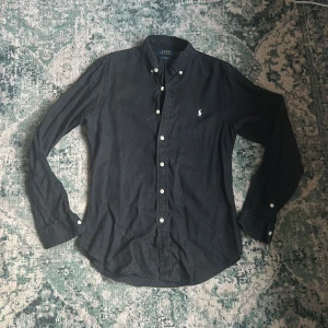 Ralph Lauren skjorta - Snygg svart skjorta från Ralph Lauren i slim fit. Skjortan har långa ärmar och knappar framtill samt en broderad logotyp på bröstet. Väldigt bra skick, priset kan prutas