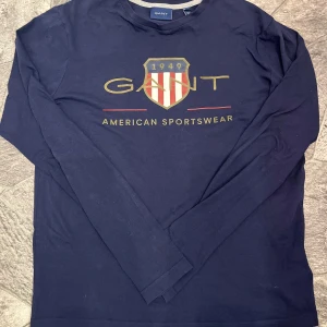 Mörkblå långärmad tröja från GANT - Säljer en stilren mörkblå långärmad tröja från GANT med tryck framtill. Tröjan har ett klassiskt GANT.tröjan är i väldigt bra skick 