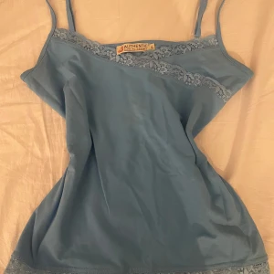 Vintage ljus blått linne  - Säljer ett blått linne med spetsdetaljer längs halsringningen och nederkanten. Linnet har smala axelband som går att justera och är perfekt för våren/sommaren. (På bilden ser tröjan lite Grå/blå ut men den är blåare i verkligheten.)