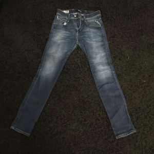 Blå jeans från Replay - Snygga blå jeans från Replay i modellen Anbass. De har en klassisk femficksdesign med dragkedja och knapp framtill. Perfekta för en avslappnad stil.