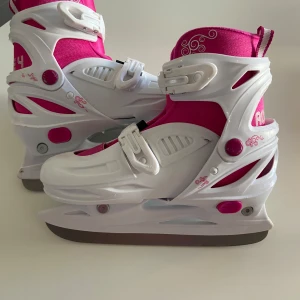 Vita och rosa skridskor - Snygga vita och rosa skridskor med justerbara spännen och dekorativa mönster. Perfekta för vinterns isäventyr. De har en stabil konstruktion och en bekväm passform. Justerbar storlek 33-36