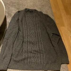 Grå stickad tröja från Hampton Republic - Säljer en snygg grå stickad tröja från Hampton Republic. Tröjan har ett klassiskt flätmönster på framsidan och ribbstickade muddar vid ärmslut och nederkant. En mysig och perfekt stickad för kyliga dagar! Stl XXL, pris kan alltid diskuteras.