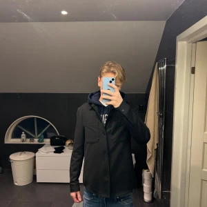 Svart overshirt - Säljer en stilren svart overshirt med knappar framtill. Den har en klassisk design med två bröstfickor och långa ärmar. Passar nästan till allt eftersom att den är svart, det är bara att höra av er vid intresse eller frågor😁🙌