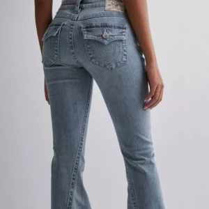 True religion joey - Säljer ett par snygga blå bootcut jeans i mycket bra skick. De har en klassisk femficksdesign med knappar och dragkedja. Perfekta för både vardag och fest! Passar bra med sneakers eller klackar för en avslappnad eller uppklädd look.