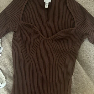 Brun ribbad tröja från H&m - Snygg brun ribbad tröja från H&m med en v-ringad design. Tröjan har trekvartsärmar och en figurnära passform som framhäver silhuetten. Perfekt för en stilren look.
