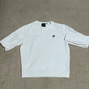 Vit sweatshirt från Lyle & Scott - Säljer en stilren vit sweatshirt från Lyle & Scott med deras ikoniska logga broderad på bröstet. Tröjan har långa ärmar och en klassisk rund halsringning. Perfekt för en avslappnad stil. Passar perfekt för M och S användare 