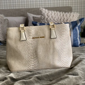 Beige axelväska med ormskinnsmönster - Snygg beige axelväska med ormskinnsmönster och gulddetaljer. Väskan har en dragkedja upptill och vita handtag. Perfekt för att ge en stilren touch till din outfit. Äkta Michael kors👜✨