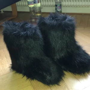Svarta pälsiga boots - Säljer ett par unika svarta boots med pälsigt yttre. Perfekta för att göra ett statement i vintergarderoben. De är både varma och stiliga, med en fluffig textur som drar blickarna till sig. OANVÄNDA