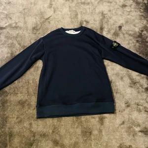 Mörkblå tröja från Stone Island - Säljer en stilren mörkblå tröja från Stone Island. Tröjan har långa ärmar och en rund halsringning. Den ikoniska Stone Island-loggan sitter på ärmen. Perfekt för en avslappnad och trendig look. Den är andvänd men inga slitningar eller fläckar! Priset är ej huggt i sten!