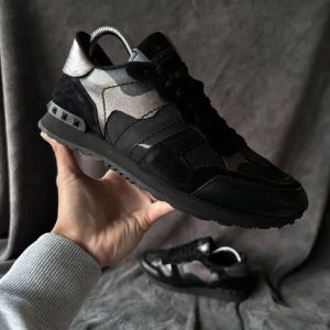Valentino Rockrunner i svart och grått - Snygga Valentino Rockrunner sneakers i svart och grått med ett coolt camouflage-mönster. Skorna har en kombination av mocka och skinn, vilket ger en lyxig känsla. De har snörning och en robust sula för extra komfort. Pris kan diskuteras lite sämre skick en på bilden skulle säga 7,5/10 passar 41