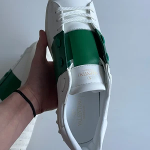 Valentino open - Snygga Valentino Garavani sneakers i vitt med gröna detaljer. Skorna har en stilren design med snörning och en mönstrad sula för extra grepp. Perfekta för en trendig look. Pris kan diskuteras. Allt og tillkommer, hör gärna av er vid frågor!