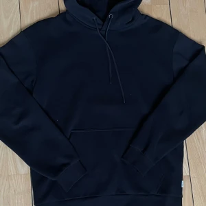 Svart Hoodie - Säljer nu denna sköna hoodie från Jack & Jonas. 8/10 skick, använd ett fåtal gånger! Skriv om ni har några funderingar eller tackar, fler bilder finns även att få! 