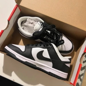 Nike Dunk i svart och vitt - Snygga Nike Dunk sneakers i klassisk svart och vit färgkombination. Skorna har en stilren design med svart snörning och en vit sula. Använda en gång!