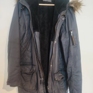 Joeama vinterjacka - Säljer en stilren grå parkajacka från Joeama med fuskpäls på huvan. Jackan har en quiltad design och flera praktiska fickor med dragkedja. Insidan är fodrad med mjukt material för extra värme. Perfekt för kyliga dagar!