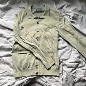 Grön kofta/cardigan från Riley - Säljer en stilren grön kofta/cardigan från Riley i herrstorlek M. Koftan har långa ärmar och knappar framtill samt två praktiska fickor. Perfekt för en avslappnad men snygg look. Den är i relativt gott skick, den är lite nopprig men annars gott skick.