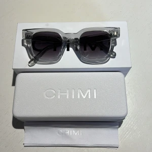 Transparenta solglasögon från Chimi (chimi 04) - Snygga transparenta solglasögon från Chimi med glittriga detaljer på bågarna. De har en fyrkantig form och mörka linser som ger en cool look. Perfekta för att lyfta din stil till nästa nivå.