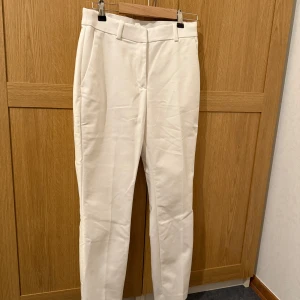 Vita kostymbyxor från H&M - Snygga vita kostymbyxor från H&M med en klassisk design. Byxorna har en rak passform och är perfekta för en stilren look. De har hällor för bälte och diskreta fickor på sidorna. Kanske passar bra till studenten?