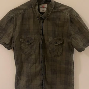 Grön rutig skjorta från Liwali Exclusive - Snygg grön rutig skjorta från Liwali Exclusive i storlek M. Skjortan har korta ärmar och två bröstfickor med knappar. Perfekt för en avslappnad stil.