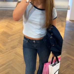 Vit och marinblå topp från Motel - Säljer en snygg vit topp med marinblå detaljer från Motel. Toppen har korta ärmar och en kontrasterande kant vid halsen och ärmsluten. Perfekt för en avslappnad stil. Det är storlek M men upplevs som S